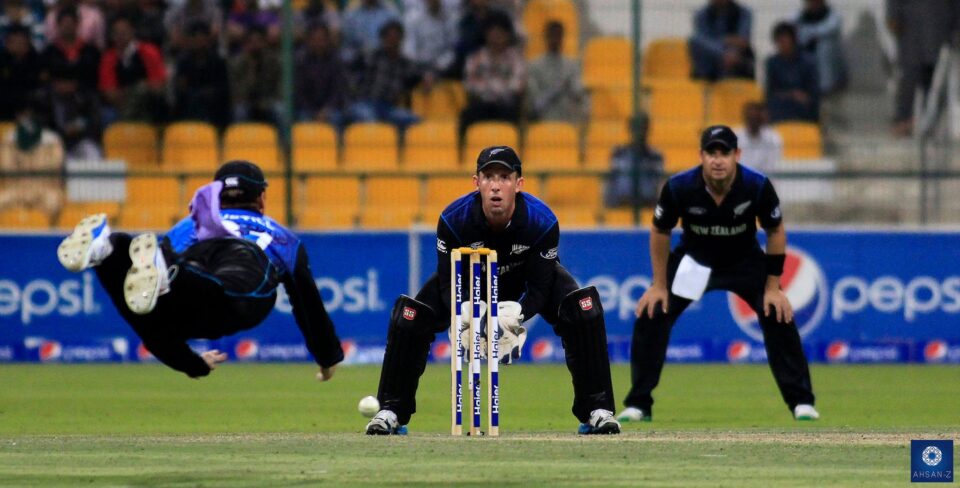 Action shot of New Zealand wicketkeeper BJ Watling, a cricket photographer's dream, poised behind the stumps as a fielder spectacularly dives for a catch, captured in a dynamic sports photograph.